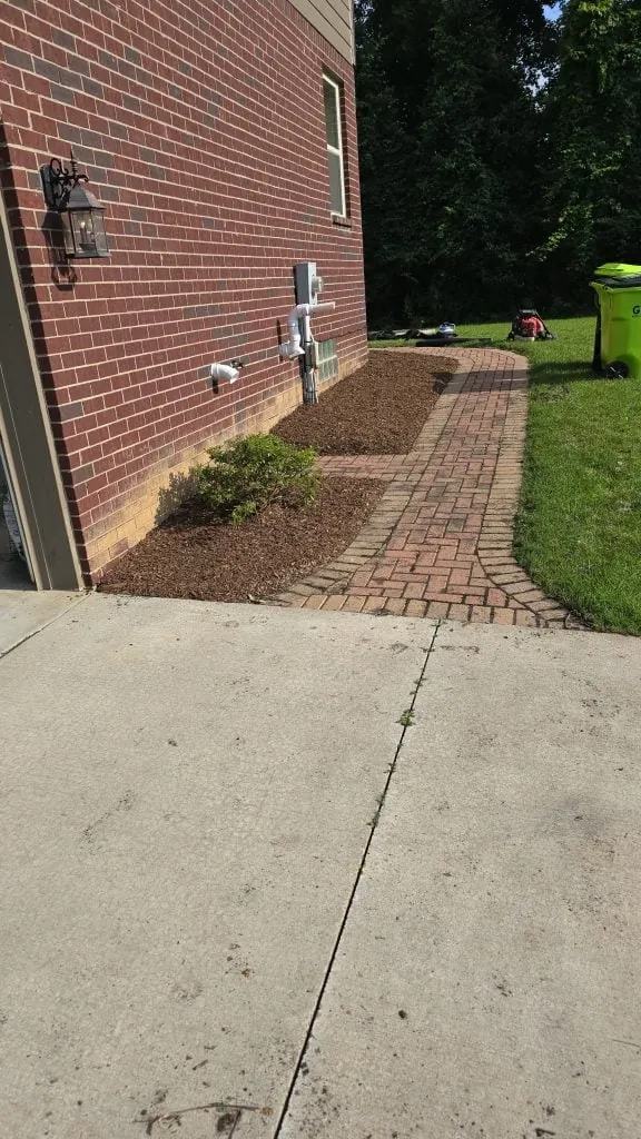 Brick paver side walkway and fresh mulch beds along the wall of a brick house